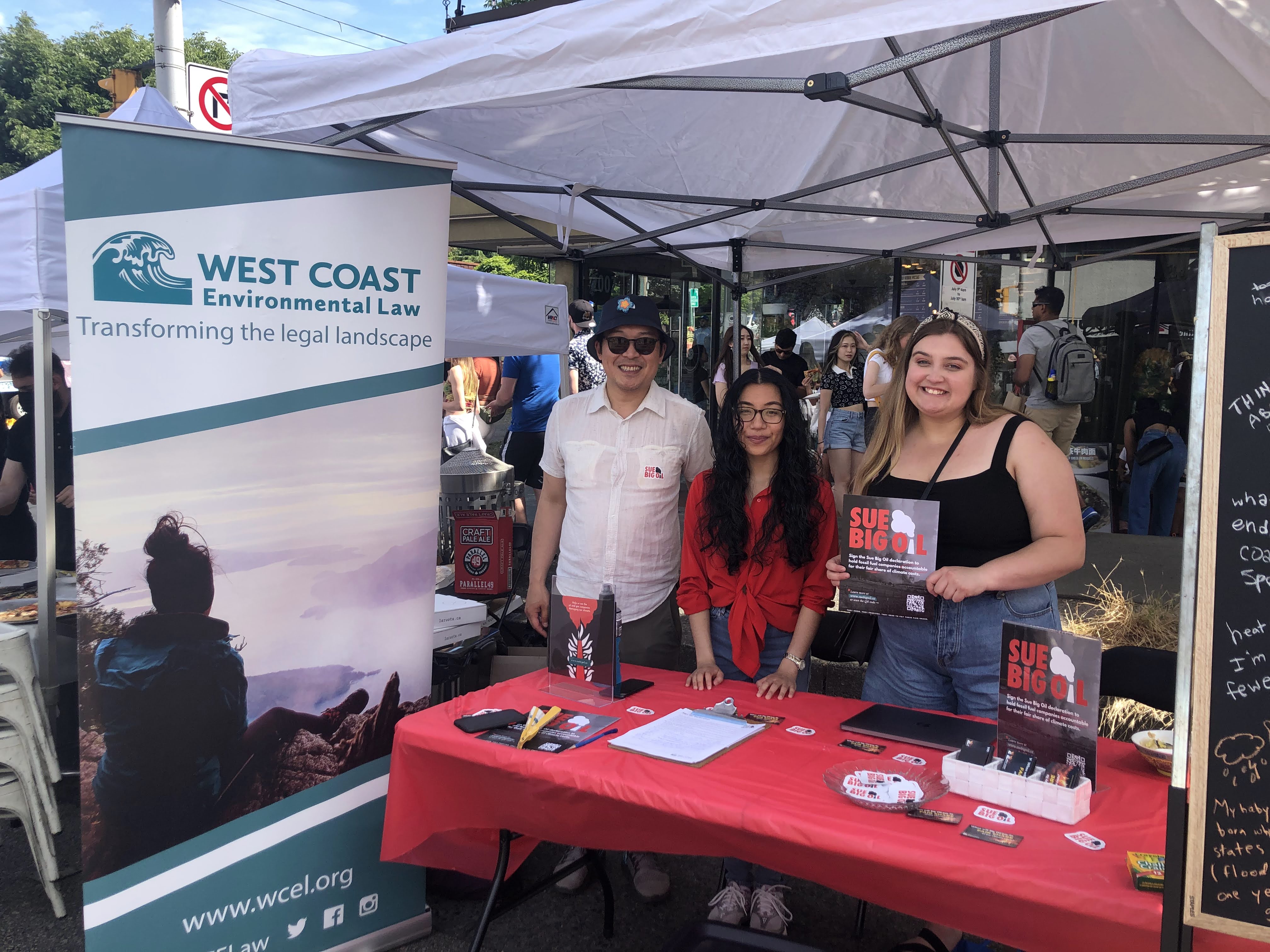 Three people standing behind an outreach booth table with red tablecloth, displaying posters and materials